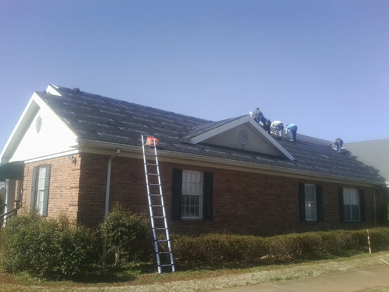 Crew tearing shingles off a brick ranch roof with a ladder set — Emergency Roof Repair work by our crew in Fleetwood