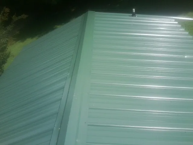 New green metal panels meeting at the ridge of a roof — Flat Roof Repair work by our crew in Fleetwood