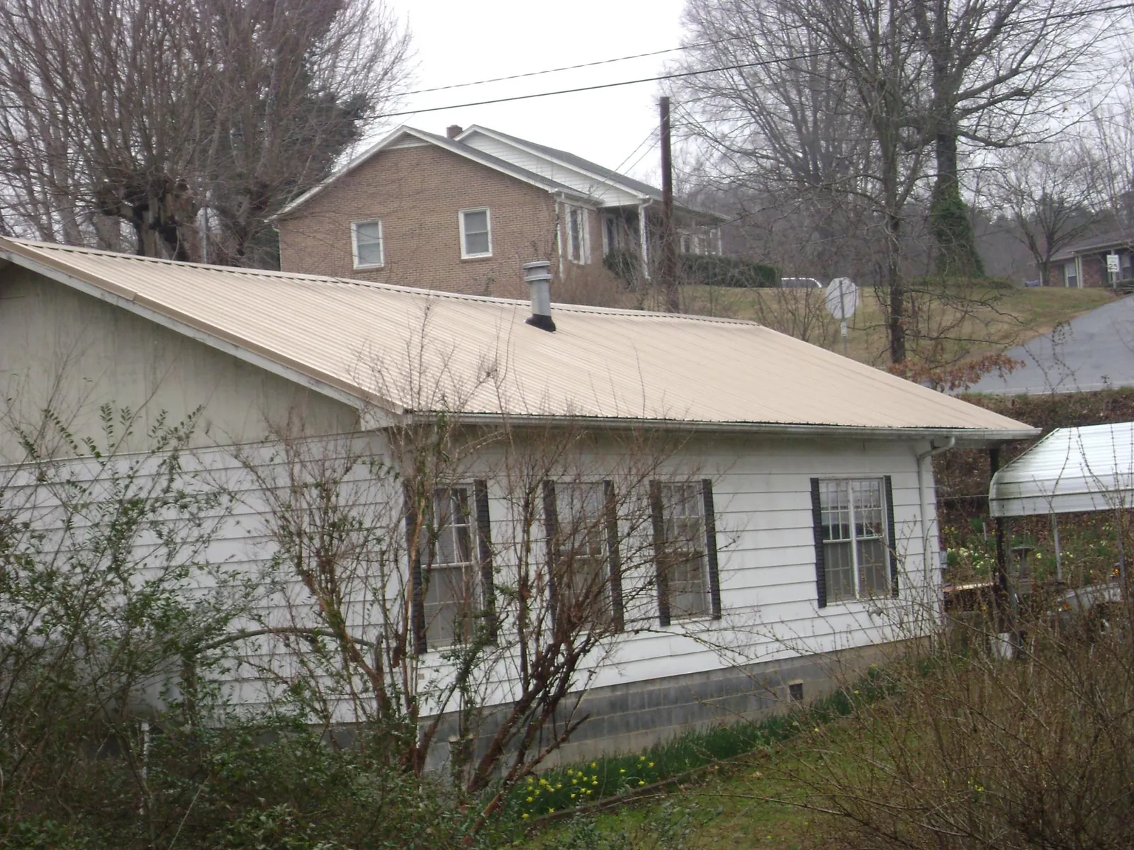 Tan metal roof on a white sided house set into a hillside — Commercial Roofing by Roofing Brothers in Fleetwood